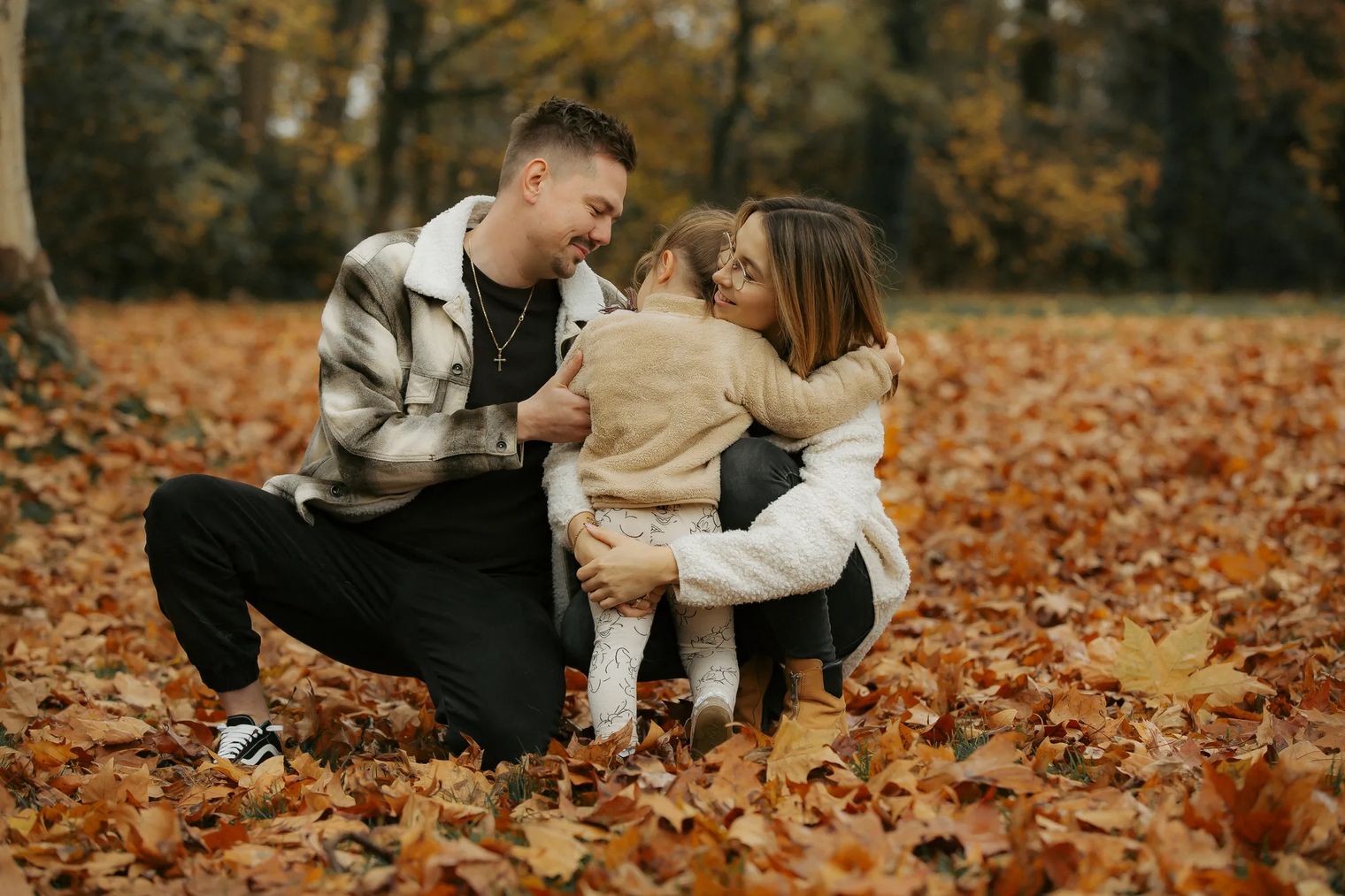 Familie mit Kleinkind im Herbstlaub, in Creme, Beige und Schwarz gekleidet